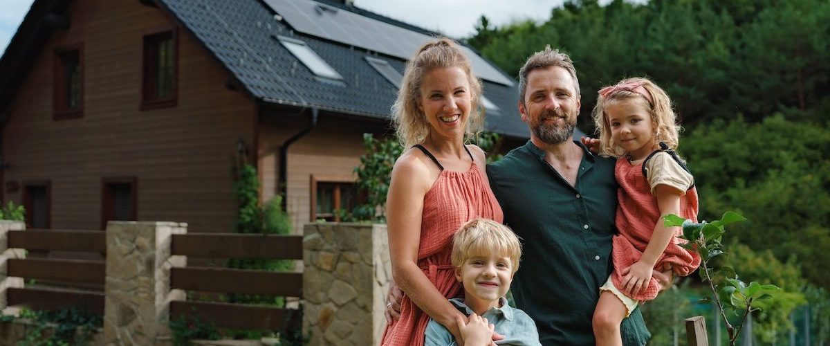 Happy family near their house with a solar panels. Alternative energy, saving resources and sustainable lifestyle concept.